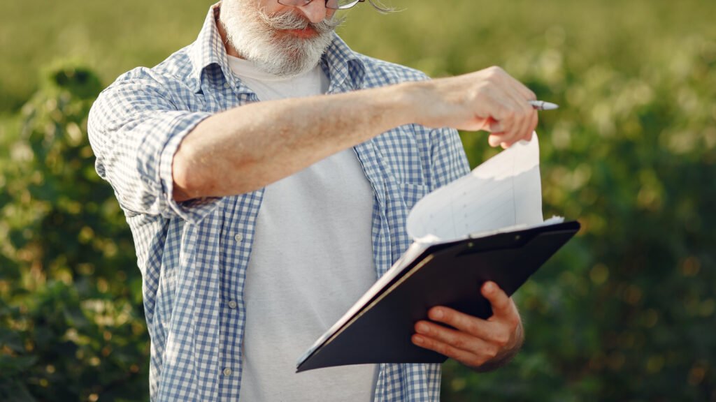 old farmer in shirt standing on field with notebook