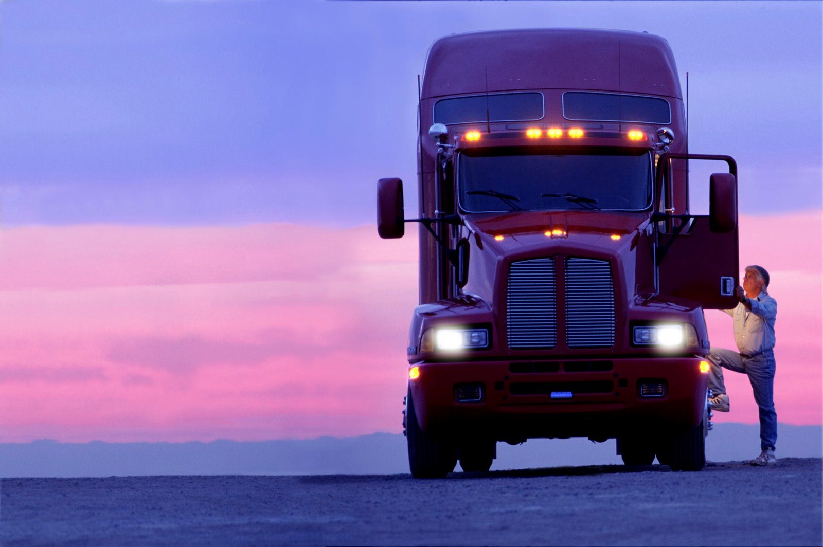 Transporte Moderno aborda garantias bancárias e continuidade da frota a silhouette of a truck driver getting into the cab of his commercial class 8 truck tractor at sunrise.