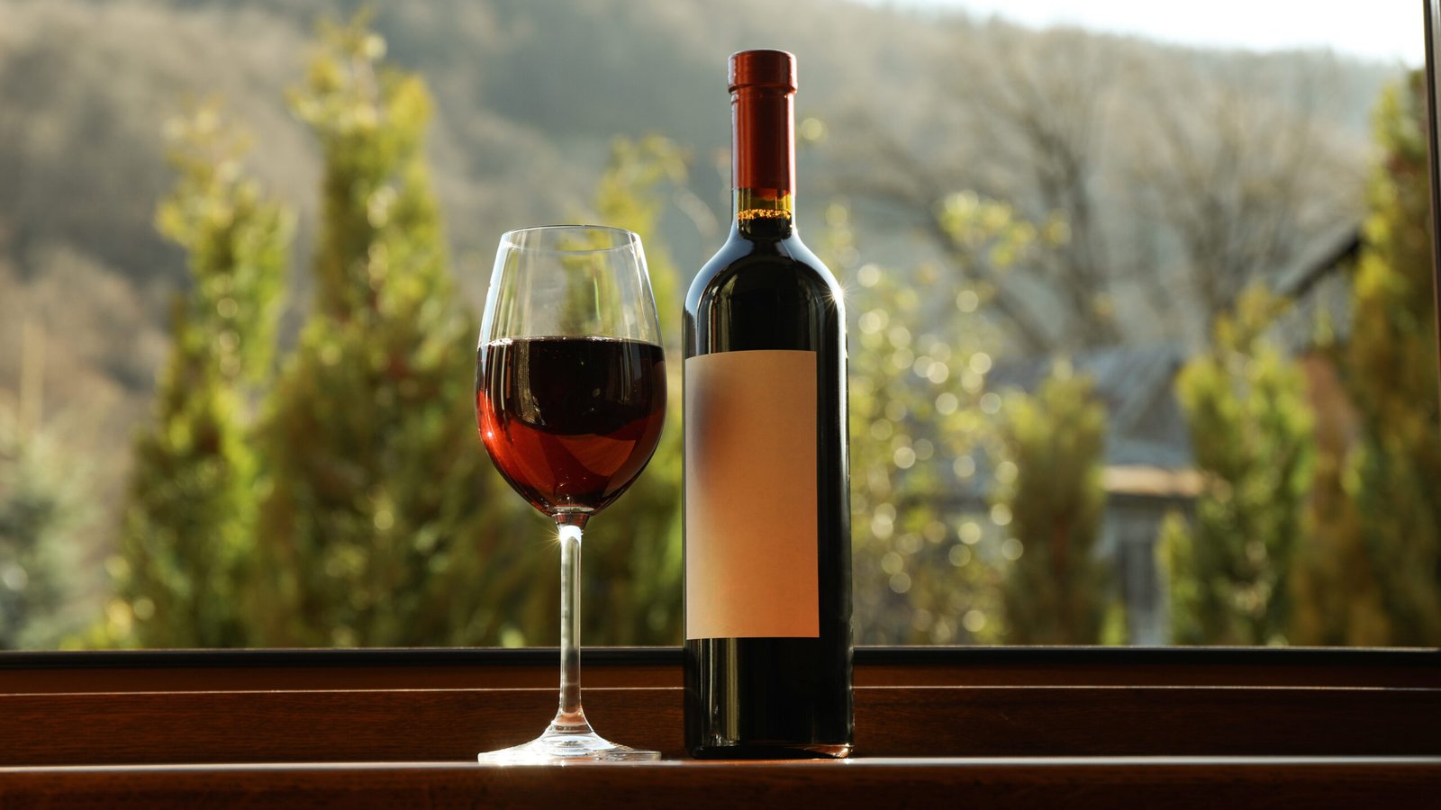 Vinho e Imposto Seletivo: cuidados para planejar a cadeia produtiva glass and bottle of wine stands on wooden windowsill